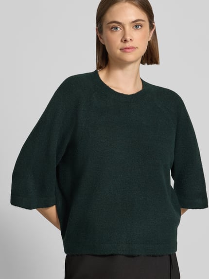 Kobieta modelka nosi ciemnozielony sweter z rękawami o dł. 3/4, model 'SIMONI' od ONLY, damski sweter, z przodu zbliżenie na górę ciała.