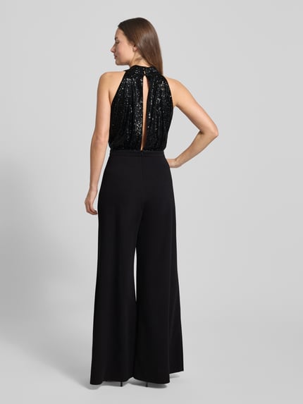 Modelka kobieca nosi Regular Fit Jumpsuit mit Pailettenbesatz od Swing, czarny, bez rękawów, z cekinami i wstążką, widok całej sylwetki z tyłu.