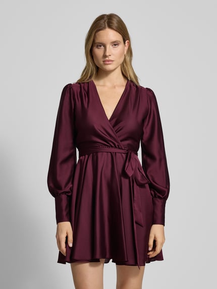 Frauenmodel trägt Cocktailkleid mit Taillengürtel von Swing in dunklem Bordeaux, glänzender Material-Mix, V-Ausschnitt, Ganzkörperansicht von vorne.
