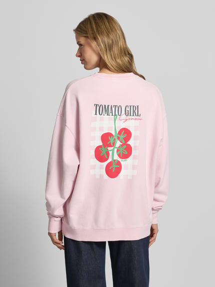 Frauenmodel trägt Oversized Sweatshirt mit rückseitigem Statement-Print von OH APRIL in Rosa mit Kirschtomatenmotiv auf Baumwolle, Ganzkörperansicht Rückansicht.