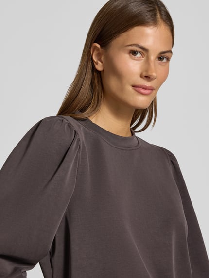 Frauenmodel trägt Sweatshirt mit Puffärmeln und Rundhalsausschnitt von Rich & Royal, glatter Micromodal-Mix, dunkles Braun, Nahaufnahme Oberkörper.