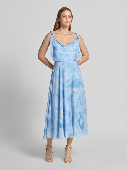 Frauenmodel trägt Knielanges Cocktailkleid mit floralem Allover-Print von Jake*s Cocktail in Hellblau mit Zierschleifen, Taillierter Passform, Blickdichtem Unterrock, Ärmellosem-Design und floraler Textur, Ganzkörperansicht von vorne. Rückenlänge bei Größe 36: 102 cm, Brustweite 40 cm.
