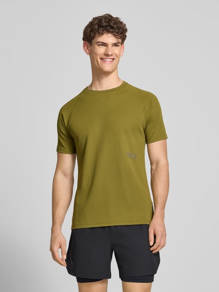 Męski model nosi T-Shirt z label-print model 'SORONA' od HALO, krój regular fit, kolor oliwkowy, z okrągłym dekoltem, całkowity widok z przodu.