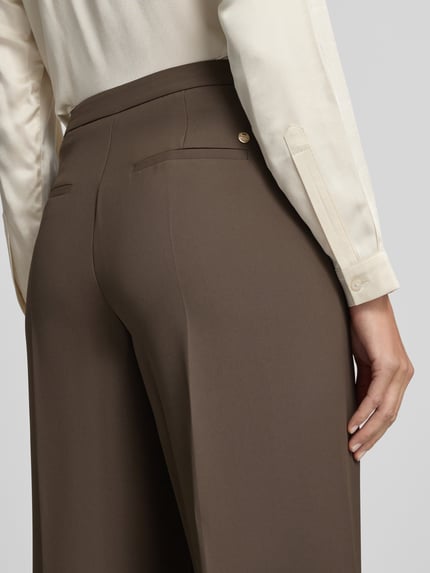 Frauenmodel trägt Straight Fit Anzughose mit Bügelfalten Modell 'Leya Miley' von MOS MOSH in Braun, glatte Textur, Nahaufnahme Rückansicht, Damen Anzughose mit Haken- und Reißverschluss, seitlichen Eingrifftaschen und Gesäßtaschen, Bundweite 45 cm, Innenbeinlänge 73 cm.