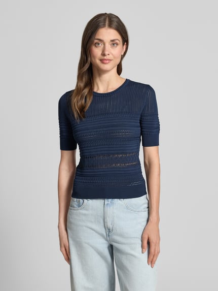 Frauenmodel trägt T-Shirt in Strick-Optik mit Rundhalsausschnitt von Guess, Material-Mix mit Viskose-Anteil, Körpernaher-Schnitt, dunkelblau, gemusterte Textur, gerippte-Abschlüsse, Ganzkörperansicht von vorne.