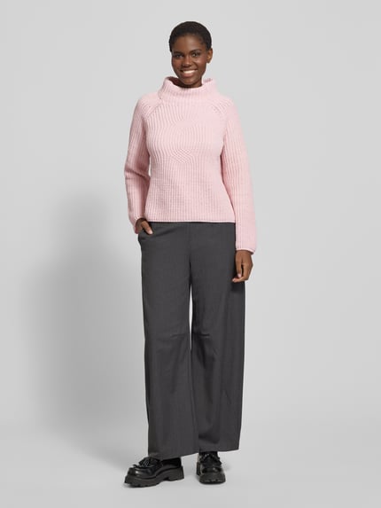 Vrouwenmodel draagt een gebreide pullover met opstaande kraag, model 'Basic Chenille' van monari in roze, regular fit grof tricot. Ruglengte maat 36: 61 cm, mouwlengte maat 36: 56 cm. Volledige lichaamsaanzicht van voren.