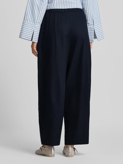 Frauenmodel trägt Culotte mit elastischem Bund und Kordelzug Modell 'Eveline' von Neo Noir in dunklem Blau, lockerer Schnitt, Ganzkörperansicht Rückansicht, Damen Culotte von Neo Noir, Loose Fit, Elastischer Bund mit Kordelzug, Bundweite bei Größe 36: 37 cm, Innenbeinlänge bei Größe 36: 72 cm.