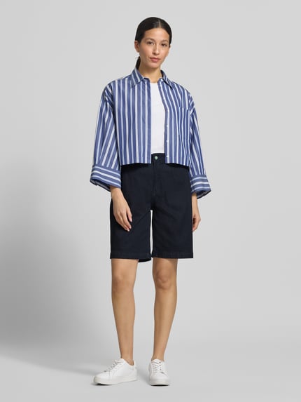 Frauenmodel trägt Chino-Shorts mit Gesäßleistentaschen von Buena Vista aus dunkelblauem Baumwoll-Mix mit Stretch-Anteil, Wide-Fit, Knopf- und Reißverschluss, seitlichen Eingrifftaschen, Bundweite bei Größe S 40 cm, Innenbeinlänge 25 cm, Ganzkörperansicht von vorne.