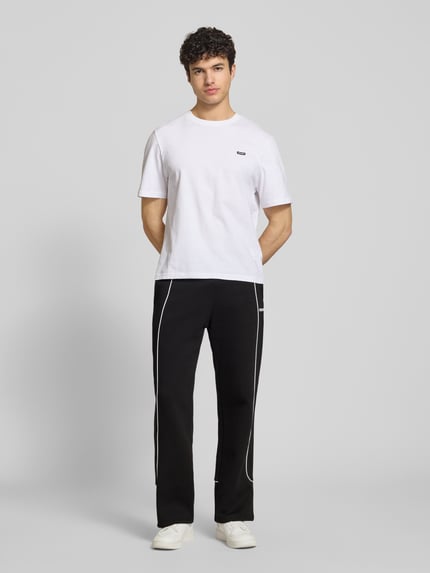 Männermodel trägt Sweatpants mit elastischem Bund und Logo von REVIEW in Schwarz mit weißen Nähten, Reine Baumwolle, Relaxed-Fit, Ganzkörperansicht von vorne.