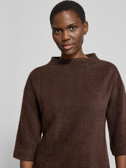 Kobiece modelka ma na sobie brązowy sweter 'Pullover mit Stehkragen und 3/4-Arm' od zero, Mieszanka materiałów z dodatkiem streczu, krój regular fit, stójka, rękaw o dł. 3/4, z przodu zbliżenie na górną część ciała.