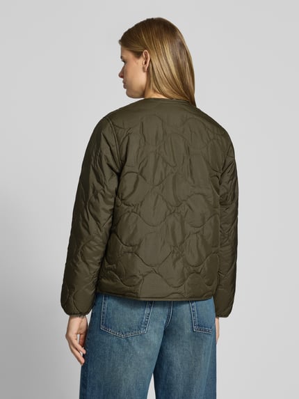 Frauenmodel trägt oliwkowozieloną kurtkę pikowaną o kroju regular fit z okrągłym dekoltem, wyhaftowane logo, listwa guzikowa, Regular Fit Steppjacke mit Label-Stitching Modell 'Skye Liner' von Carhartt Work In Progress, długość tyłu w rozmiarze S: 61 cm, szerokość ramion w rozmiarze S: 41 cm, szerokość w rozmiarze S: 54 cm, długość rękawów w rozmiarze S: 61 cm, widok całej sylwetki z tyłu.