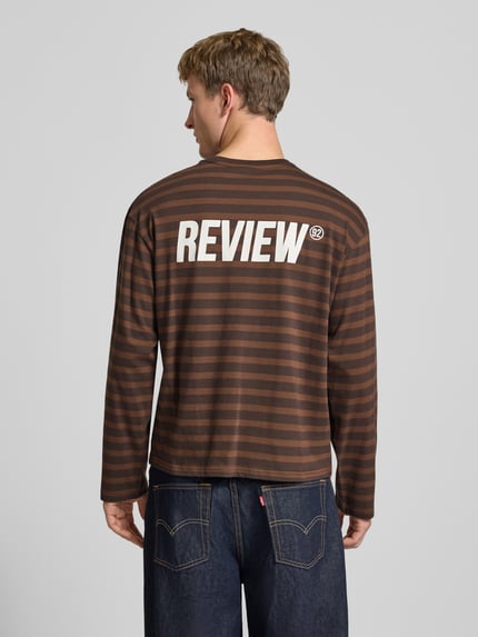 Männermodel trägt Gestreiftes Langarmshirt mit Logoprint vorne und hinten von REVIEW, braune und schwarze Streifen, Rückansicht, Ganzkörperansicht Rückansicht. Reine Baumwolle, Regular Fit, Rundhalsausschnitt, Rückenlänge bei Größe M 61 cm.