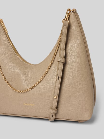 Produktfoto, Handtasche mit Label-Detail von CK Calvin Klein in Beige mit goldfarbenem Schulterriemen, strukturierte Oberfläche, Kontext Damen Handtasche mit Reißverschluss, Innenfach, Maße 24x27x11 cm, Riemenlänge 68 cm