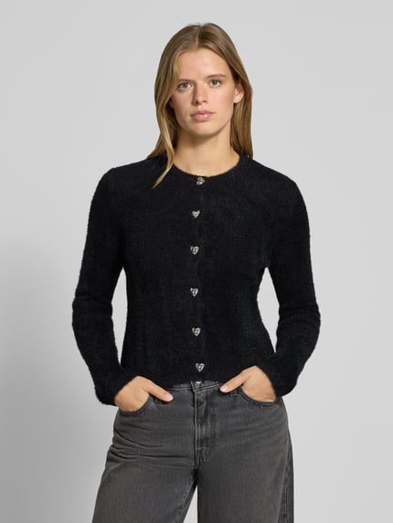 Frauenmodel trägt Strickjacke mit Herzknöpfen von ONLY in Schwarz mit silbernen Knöpfen und weicher Struktur, Ganzkörperansicht von vorne.