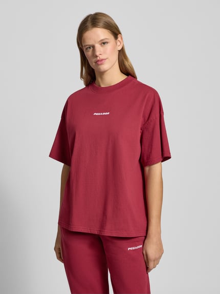 Frauenmodel trägt Oversized T-Shirt mit Logo Modell 'BRACY' von Pegador aus reiner Baumwolle in Dunkelrot, Ganzkörperansicht von vorne.