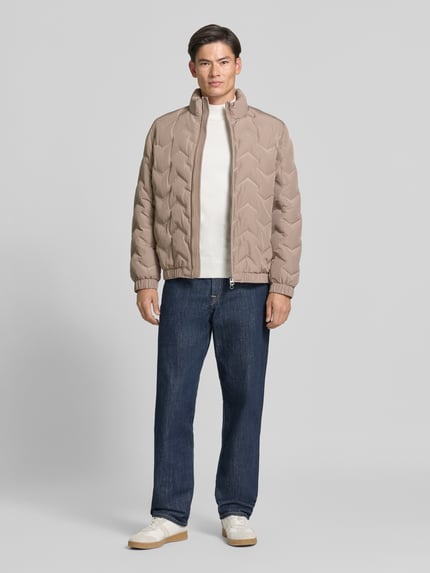 Männermodel trägt Steppjacke mit Stehkragen und Reißverschlusstaschen von Antony Morato, krój regular fit, beżowy kolor, Ganzkörperansicht von vorne, szerokość w rozmiarze 50: 59 cm, długość tyłu: 71 cm, szerokość ramion: 50 cm, długość rękawa: 66 cm.