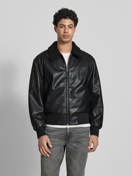 Mężczyznamodel nosi Regular Fit Jacke in Leder-Optik mit Umlegekragen von Calvin Klein Jeans, kolor czarny, krój regular fit, wykładany kołnierz, zamek błyskawiczny dwustronny, detal z logo, wpuszczane kieszenie, elastyczne wykończenia, długość tyłu w rozmiarze M: 64 cm, szerokość ramion w rozmiarze M: 51 cm, szerokość klatki piersiowej w rozmiarze M: 62 cm, długość rękawów w rozmiarze M: 63 cm, gładka tekstura, widok całej sylwetki z przodu