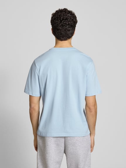 Männermodel trägt lichtblauw T-shirt met logo en ronde hals van REVIEW, katoen- en viscosemix, regular fit, ruglengte maat M 64 cm. Ganzkörperansicht Rückansicht.