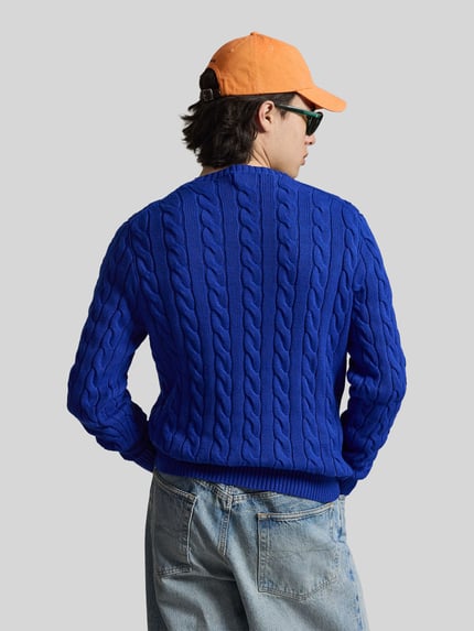 Männermodel trägt Regular Fit Strickpullover aus reiner Baumwolle von Polo Ralph Lauren in Optik: Unifarben, Strickoptik, Zopfmuster, Logo-Detail, Rundhals, Langarm, Rumpfabschluss gerippt, Materialverarbeitung: Strick, Material: reine Baumwolle, Ganzkörperansicht Rückansicht.