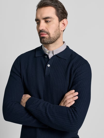 Męski model nosi Strickpullover mit Polokragen von Christian Berg Men; granatowa bawełna, regular fit, krótka lista guzików, tekstura w prążki, z przodu półzbliżenie.