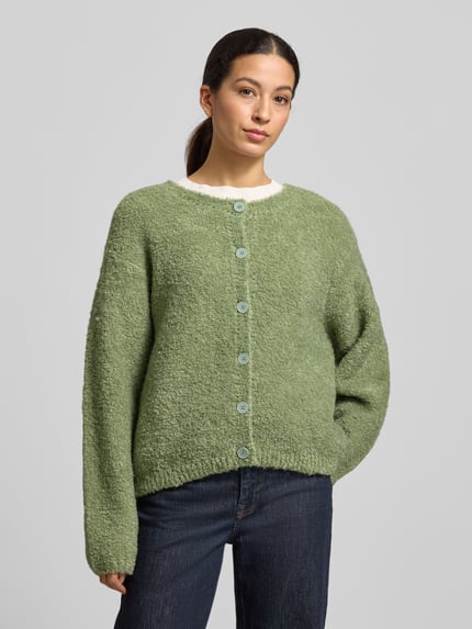 Frauenmodel trägt locker geschnittene, grüne Strickjacke mit Knopfleiste Modell 'ZOLLY' von American Vintage, Rundhalsausschnitt, gerippte Abschlüsse, Lanawoll-Alpaka-Mix, Nahaufnahme Oberkörper.