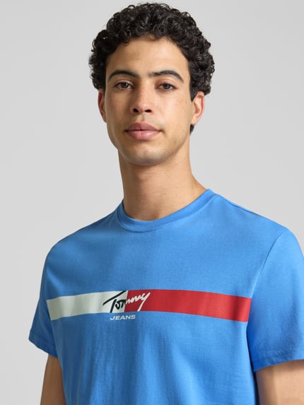 Mannenmodel draagt Regular Fit T-Shirt aus reiner Baumwolle van Tommy Jeans in effen blauw met label print, ronde hals, korte mouw, jersey van puur katoen, Nahaufnahme bovenlichaam.