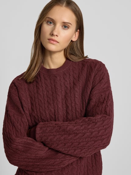 Frauenmodel trägt Oversized Fit Strickpullover mit Zopfmuster von REVIEW in Bordeaux, elastischer Material-Mix, Nahaufnahme Oberkörper.