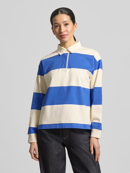 Frauenmodel trägt Regular Fit Langarm-Poloshirt mit verdeckter Knopfleiste von Gant, Baumwolle, Polokragen, in Creme und Blau, Ganzkörperansicht von vorne.