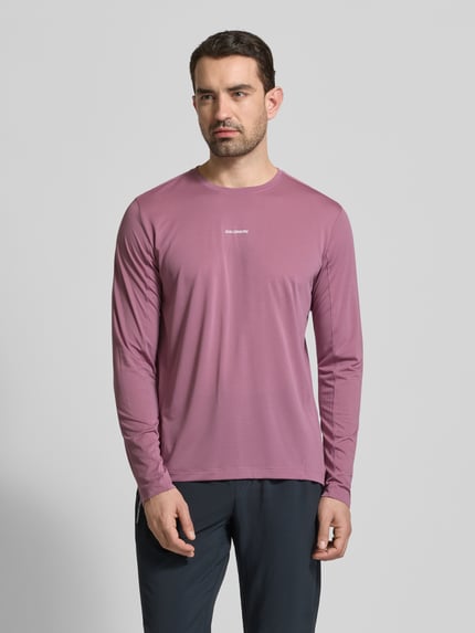 Männermodel trägt Funktionsshirt mit Logo und Rundhalsausschnitt von Salomon in Altrosa, Regular Fit, Langarm, glatte Textur, Ganzkörperansicht von vorne.
