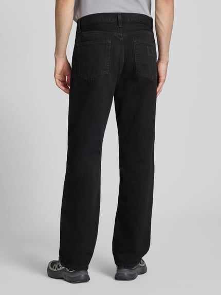 Mężczyzna nosi Wide Fit Jeans im 5-Pocket-Design Modell 'Aaron' von Carhartt Work In Progress, czarny denim, czysta bawełna, szerokie nogawki, Szerokość w rozmiarze 32: 44 cm, długość wewnętrzna nogawki 80 cm, guziki i zamek, widok całej sylwetki z tyłu.