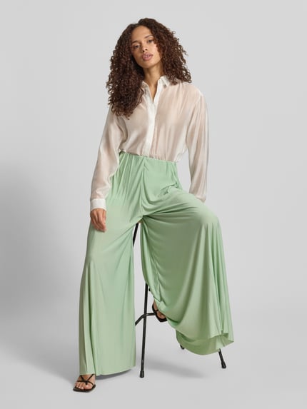 Vrouwenmodel draagt stoffen broek van satijn, wide leg fit, model 'Samantha' van GUIDO MARIA KRETSCHMER WOMAN, plissévouwen, elastische band, lichtgroen, gladde textuur, bandwijdte maat 36: 34 cm, binnenbeenlengte maat 36: 73 cm. Ganzkörperansicht von vorne.