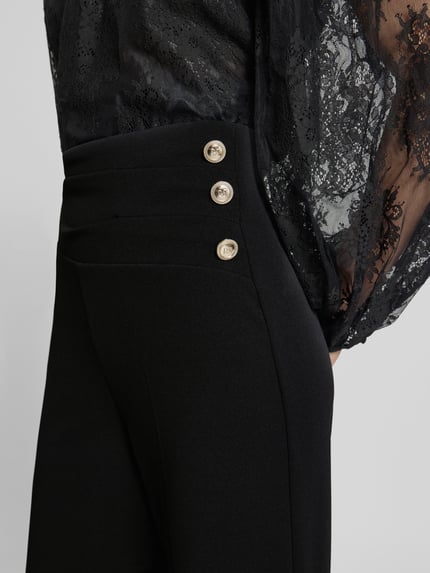 Frauenmodel trägt Flared Cut Hose mit Knöpfen von Rinascimento, schwarzer Material-Mix mit Stretch, Nahaufnahme Oberkörper