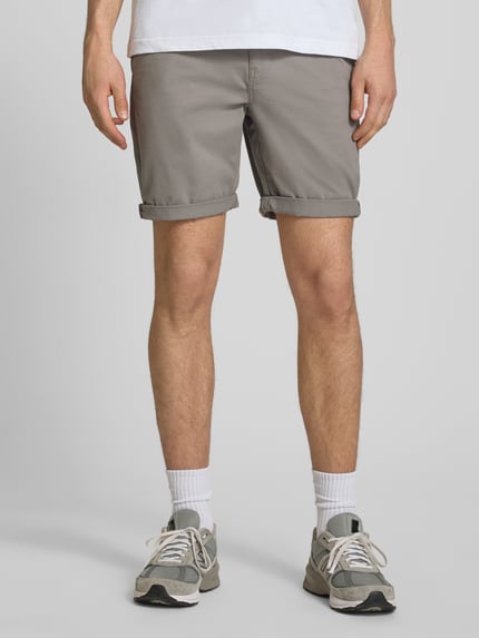 Männermodel trägt Regular Fit Shorts mit Münztasche von Superdry in Beige, Baumwoll-Mix, mit Gesäßtaschen und Knopf-Reißverschluss, Ganzkörperansicht von vorne.