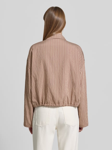 Vrouwenmodel draagt Boxy fit blouse uit viscosemix Model 'FIONEL' van DRYKORN met streepmotief en tunnelkoord, ruglengte maat 36: 55 cm, mouwlengte maat 36: 53 cm, overhemdkraag, verborgen knoopsluiting, kleur bruin-beige, structuur glad, geheel achteraanzicht.