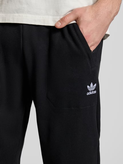 Männermodel trägt Straight Fit Sweatpants mit elastischem Bund Modell 'Essentials' von adidas Originals, schwarzer Strukturstoff, Nahaufnahme Oberkörper.