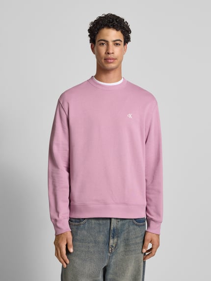Männermodel trägt Sweatshirt aus reiner Baumwolle von Calvin Klein Jeans in Rosa, gerader Schnitt, Rundhalsausschnitt, Label-Stitching, gerippte Abschlüsse, Jeans, Ganzkörperansicht von vorne.