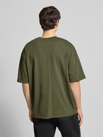 Männermodel draagt Oversized T-Shirt mit Label-Stitching van Pegador in olijfgroen, pure katoen, geribde ronde hals, geheel lichaam achteraanzicht.