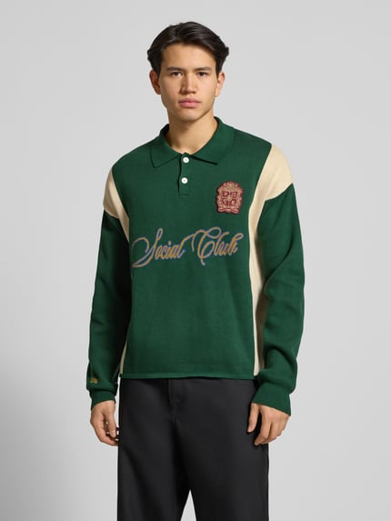 Männermodel trägt Strickpullover mit Polokragen und Label-Patch von PROHIBITED, grün-beige, Relaxed-Fit, reine Baumwolle, Nahaufnahme Oberkörper.
