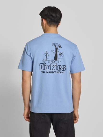 Męski model nosi t-shirt z nadrukiem z logo model 'FAIRLAWN' od Dickies, bawełna, krój regular fit, okrągły dekolt, długość tyłu w rozmiarze M 72 cm, jasnoniebieski, widok całej sylwetki z tyłu