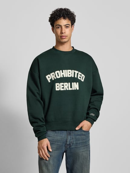 Männermodel trägt Oversized Sweatshirt mit Label-Detail von PROHIBITED, dunkelgrün, Baumwoll-Mix, gerippte Abschlüsse, Rundhalsausschnitt, Ganzkörperansicht von vorne.