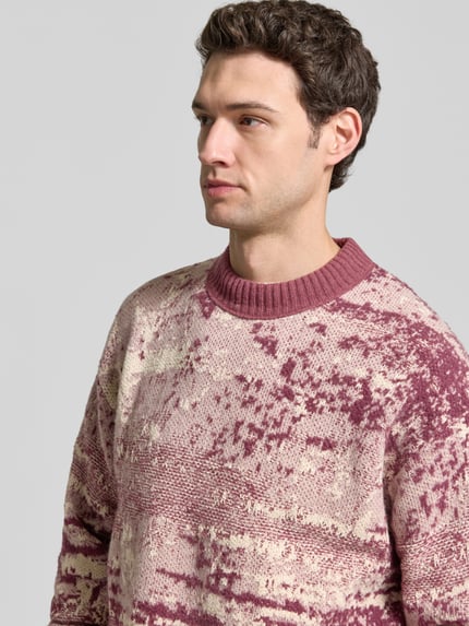Männermodel trägt Pullover mit geripptem Rundhals Modell 'Kastet' von BOSS Orange, abstraktes Allover-Muster, Nahaufnahme Oberkörper.