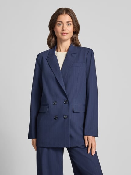Frauenmodel trägt Blazer mit Pattentaschen Modell 'Lana' von My Essential Wardrobe in Dunkelblau mit Reverskragen und Doppelknopf, Ganzkörperansicht von vorne. Boxy Fit, Material-Mix mit Viskose-Anteil, dezentes Nadelstreifenmuster, Brustleistentasche, glatte Oberfläche.