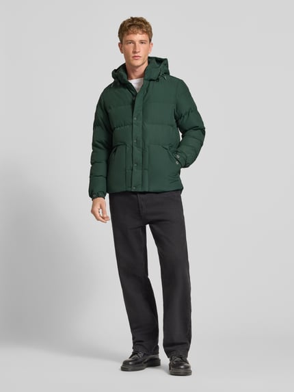 Männermodel trägt dunkelgrüne Jacke mit Kapuze Modell 'CLASSIC EVEREST' von Superdry, gerade Passform, Ganzkörperansicht von vorne.