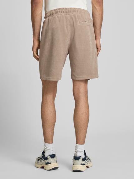Männermodel trägt Relaxed Fit Shorts mit Strukturmuster Modell 'Lagos' von Pegador in Beige mit elastischem Bund, Ganzkörperansicht Rückansicht.