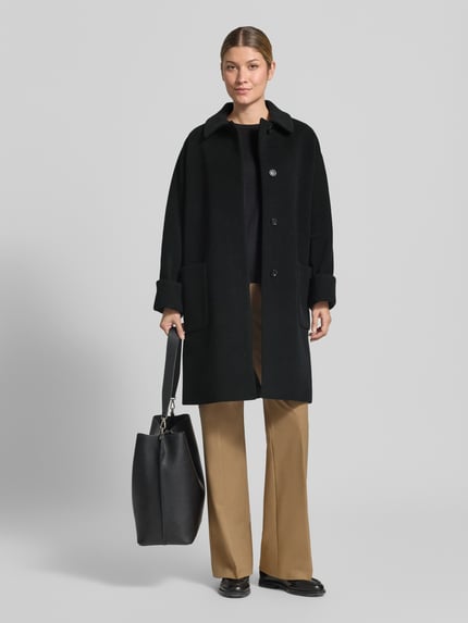 Frauenmodel trägt Mantel aus Lanawolle-Mix mit aufgesetzten Taschen von ICONS Cinzia Rocca in Schwarz, Knopfverschluss, Umlegekragen, Ganzkörperansicht von vorne.