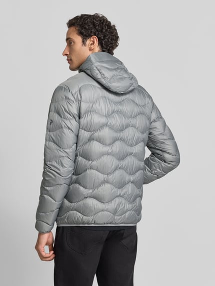 Männermodel trägt Slim Fit Steppjacke mit Kapuze Modell 'Helium' von Peak Performance in Grau, texturierte Oberfläche, Ganzkörperansicht Rückansicht