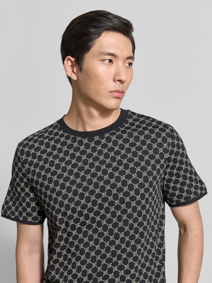 Männermodel trägt T-Shirt mit Logo-Muster und Rundhalsausschnitt von JOOP! Collection aus Baumwoll-Lyocell-Mix, Regular-Fit, Nahaufnahme Oberkörper.