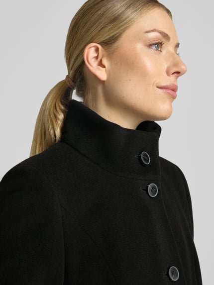 Frauenmodel trägt Regular Fit Mantel aus Woll-Mix mit Kaschmir-Anteil von FUCHS SCHMITT, schlichter schwarzer Stoff und Stehkragen, Nahaufnahme Oberkörper.