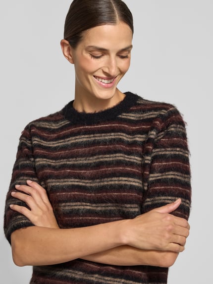 Vrouwenmodel draagt Slim Fit Strickpullover aus Polyacryl-Mix mit Streifenmuster van OPUS in bruin, zwart en beige tinten, close-up bovenlichaam.