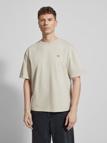 Männermodel trägt T-Shirt mit Logo-Print Modell 'Gary' von Wood Wood in Beige, gerader Schnitt, reine Baumwolle, Nahaufnahme Oberkörper.